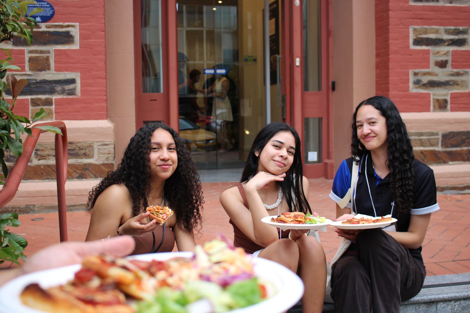 Three friends eating dinner on the steps outside the Centre